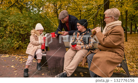 Parents and kids relaxing on park bench with sandwiches and hot drinks Parents and kids relaxing on park bench with sandwiches and hot drinks 132776156