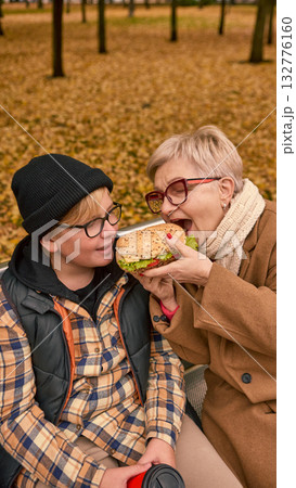 Grandmother sharing sandwich with grandson in autumn park Grandmother sharing sandwich with grandson in autumn park 132776160
