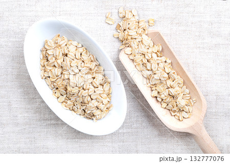 Rolled oats, thick-rolled and old-fashioned oats, in white bowl and grain scoop, on linen. Dehusked and steamed oat groats, rolled into flakes under heavy rollers, stabilized through lightly toasting. Rolled oats, thick-rolled and old-fashioned oats, in white bowl and grain scoop, on linen. Dehusked and steamed oat groats, rolled into flakes under heavy rollers, stabilized through lightly toasting. 132777076