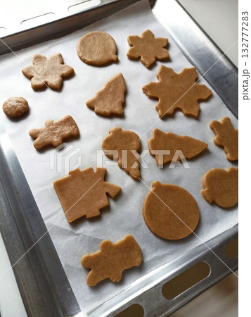 Unbaked gingerbread cookies in festive shapes arranged on parchment paper on a metal baking tray. Concept of homemade holiday baking and Christmas family traditions Unbaked gingerbread cookies in festive shapes arranged on parchment paper on a metal baking tray. Concept of homemade holiday baking and Christmas family traditions 132777283