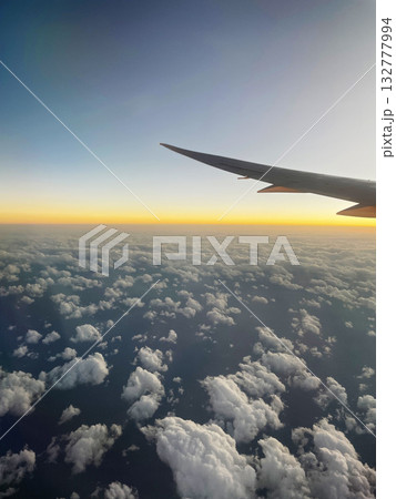 夕焼けの空と雲の上を飛ぶ飛行機の翼 132777994