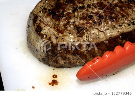 Close up of seasoned cooked steak resting on a white chopping board Close up of seasoned cooked steak resting on a white chopping board 132779349