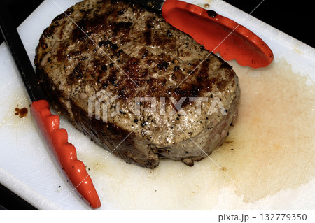 Close up of seasoned cooked steak resting on a white chopping board Close up of seasoned cooked steak resting on a white chopping board 132779350
