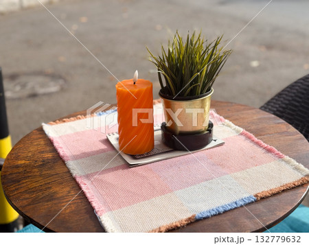 Orange candle and potted plant on a cafe terrace table. Simplicity, light and aesthetic calm in outdoor lifestyle design. 132779632
