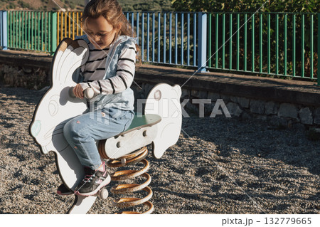 Happy child playing outdoors on a spring swing in the shape of an animal character Happy child playing outdoors on a spring swing in the shape of an animal character 132779665