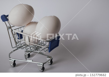 White chicken egg in a tiny shopping cart on a clean white background White chicken egg in a tiny shopping cart on a clean white background 132779682