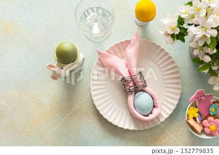A vibrant Easter table setting features a beautifully arranged plate with a wrapped egg, decorated cookies, and fresh flowers, creating a joyful atmosphere for the holiday gathering 132779835