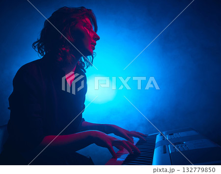 Female keyboardist playing under cinematic blue stage lighting 132779850