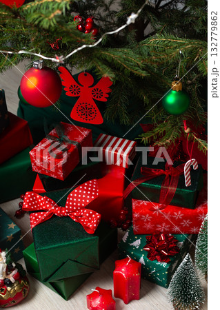 A festive display of green and red gift boxes under a beautifully decorated Christmas tree, complemented by candles and traditional ornaments, evoking warmth and holiday cheer 132779862