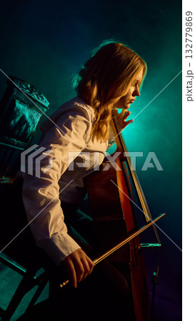 Side view of female cellist performing on stage with teal lighting 132779869
