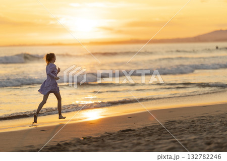 Woman running barefoot along beach enjoying golden hour freedom 132782246