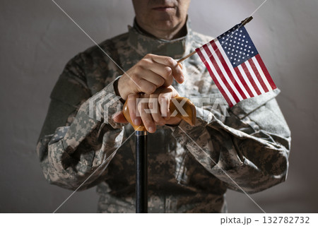 Soldier in camouflage uniform holding a cane and us flag symbolizing veteran support and resilience Soldier in camouflage uniform holding a cane and us flag symbolizing veteran support and resilience 132782732
