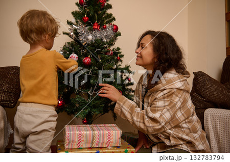 Mother And Child Decorating The Christmas Tree At Home With Gifts Underneath 132783794
