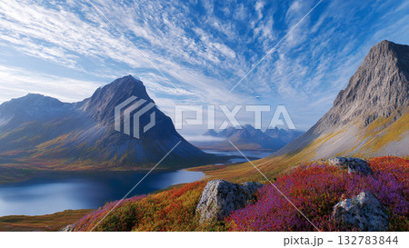 Vibrant Mountain Landscape with Colorful Alpine Flowers Overlooking Clear Lake and Expansive Mountain Ranges under a Dynamic Sky 132783844