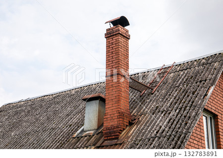 Close-up of a sloped roof with weathered corrugated sheets, a tall red brick chimney 132783891