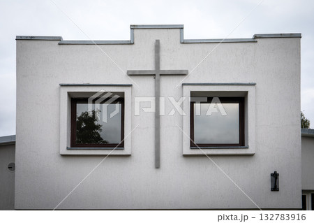 Front view of a minimalist church building facade featuring a large cross between two square windows 132783916
