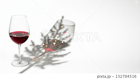 Glass of red wine on white background casting a magical Christmas tree-shaped shadow with tiny glowing lights. Glass of red wine on white background casting a magical Christmas tree-shaped shadow with tiny glowing lights. 132784516