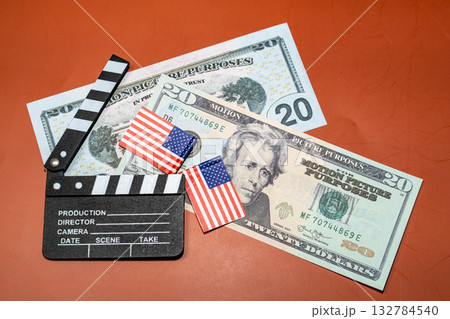 A film clapper board rests alongside American currency and small flags, hinting at movie finance and patriotic filmmaking. 132784540