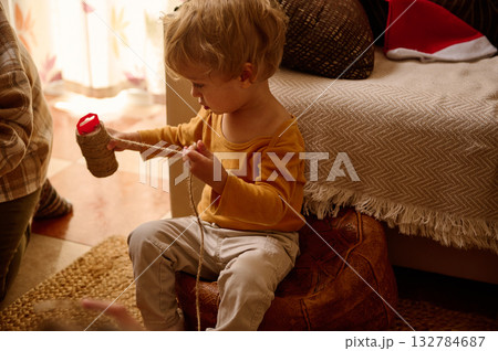 Young Child Playing With String And Yarn In Cozy Home Evening Scene 132784687