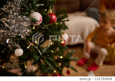 Cozy Christmas Tree With Ornaments In Foreground And A Child In Soft Focus In The Background Cozy Christmas Tree With Ornaments In Foreground And A Child In Soft Focus In The Background 132784688