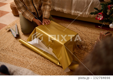 Person Wrapping Gold Gift Under Christmas Tree In Cozy Home Setting Person Wrapping Gold Gift Under Christmas Tree In Cozy Home Setting 132784698