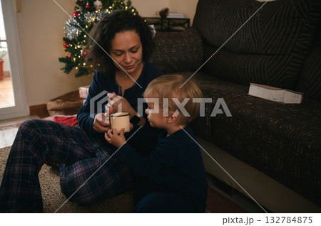 Mother And Child Share Warm Moment With Mug Near Christmas Tree In Cozy Living Room 132784875