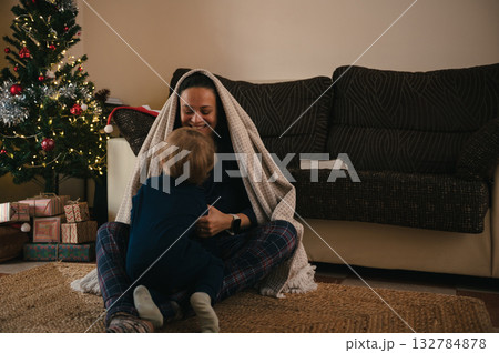 Cherished Family Moment: Mother Beneath Blanket With Baby By Christmas Tree And Gifts Cherished Family Moment: Mother Beneath Blanket With Baby By Christmas Tree And Gifts 132784878