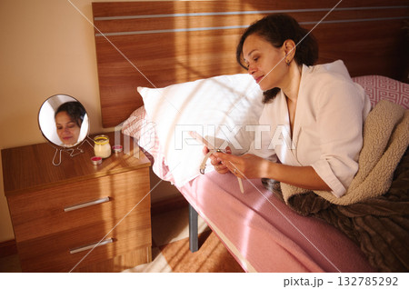 Woman Relaxing In Bed With Smartphone By Mirror And Nightstand At Home Woman Relaxing In Bed With Smartphone By Mirror And Nightstand At Home 132785292