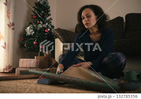Woman Wrapping Christmas Gifts Beside A Tree In Cozy Living Room With Presents 132785356
