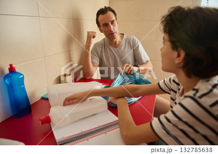 Man And Woman Pack Supplies At Red Table In Kitchen, Discussing Items While Preparing Bags Man And Woman Pack Supplies At Red Table In Kitchen, Discussing Items While Preparing Bags 132785638