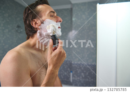 Man Shaving With Razor and Foam in Bathroom Mirror - Grooming Routine Close-Up 132785785