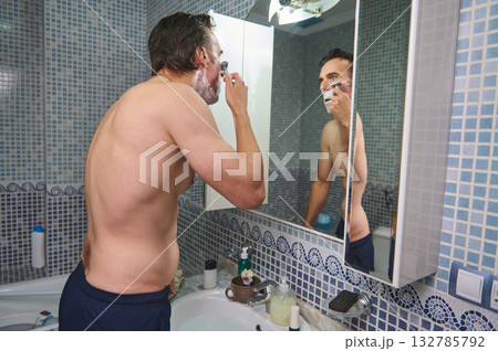 Man Shaving in Bathroom Mirror During Morning Routine, Grooming Personal Care Moment Man Shaving in Bathroom Mirror During Morning Routine, Grooming Personal Care Moment 132785792