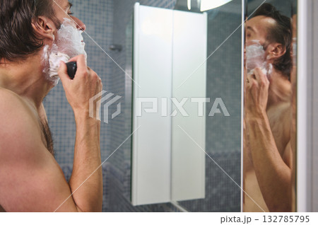 Man Shaving in Bathroom With Foamy Beard, Reflected in Mirror, Close-Up At Home Man Shaving in Bathroom With Foamy Beard, Reflected in Mirror, Close-Up At Home 132785795