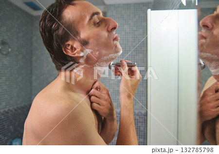 Man Shaving Facial Hair In Front Of Mirror In Bathroom, Getting Ready For Day Man Shaving Facial Hair In Front Of Mirror In Bathroom, Getting Ready For Day 132785798