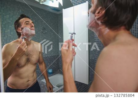 Man Shaving in Bathroom Mirror, Morning Grooming Routine with Shaving Foam 132785804
