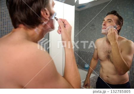 Man Shaving in Mirror at Home: Grooming Ritual in a Modern Bathroom Setting Man Shaving in Mirror at Home: Grooming Ritual in a Modern Bathroom Setting 132785805