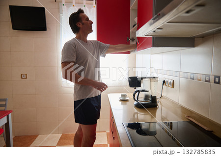 Man Reaches Into Red Kitchen Cabinet Over Coffee Station In Modern Home Kitchen 132785835