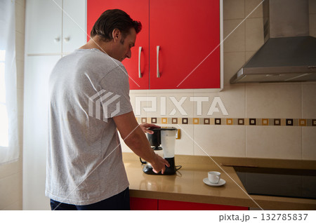 Man Brewing Coffee in Modern Kitchen With Red Cabinets and Coffee Maker 132785837