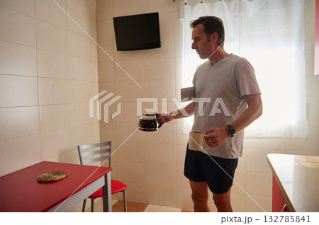 Man In Kitchen Pouring Coffee From Pot While Holding Mug During Morning Routine 132785841