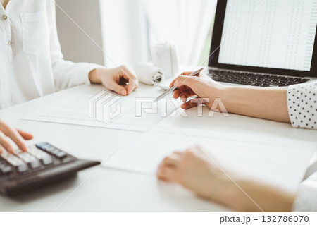 Two accountants using a laptop computer and calculator for counting taxes at white desk in office. Teamwork in business audit and finance Two accountants using a laptop computer and calculator for counting taxes at white desk in office. Teamwork in business audit and finance 132786070