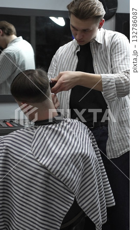 Professional barber carefully trimming customer's hair with electric clipper, providing a stylish and precise haircut in a modern barbershop environment 132786087