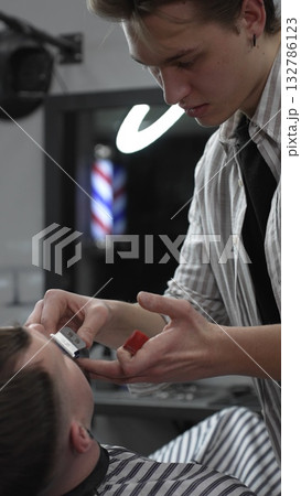 Professional barber trimming customer's hair with electric clipper, focusing on precise nape grooming within contemporary barbershop interior design Professional barber trimming customer's hair with electric clipper, focusing on precise nape grooming within contemporary barbershop interior design 132786123