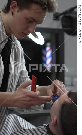 Professional barber trimming customer's hair with electric clipper, focusing on precise nape grooming within contemporary barbershop interior design Professional barber trimming customer's hair with electric clipper, focusing on precise nape grooming within contemporary barbershop interior design 132786173