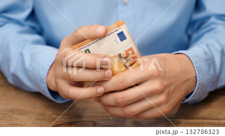 Close-up of male hands holds euro banknotes. Man in blue shirt holding European currency. Financial concept background for salary, savings or budget planning. 132786323