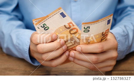 Close-up of male hands counting euro banknotes. Man in blue shirt counting money, 50 euro bills. Financial concept background for salary, savings or budget planning. Investor counting money. Close-up of male hands counting euro banknotes. Man in blue shirt counting money, 50 euro bills. Financial concept background for salary, savings or budget planning. Investor counting money. 132786327