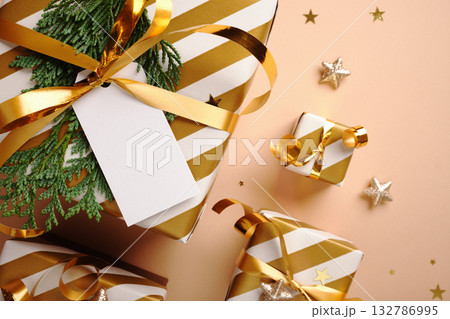 Close-up of white and gold striped gifts with blank label on beige background. Selective focus. Copy space. Close-up of white and gold striped gifts with blank label on beige background. Selective focus. Copy space. 132786995