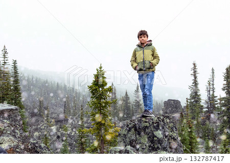 Boy stands among big rocks geological formation in the mountains. 132787417