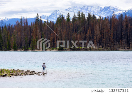 Teen hiker at the lake among mountain peaks and burnt forest. 132787531