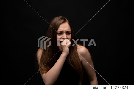 Fearful emotion of young woman covering mouth with hand in black top on dark background 132788249