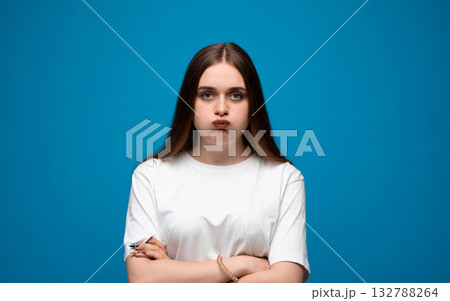 Annoyed emotion of young woman with puffed cheeks in white t-shirt on blue background Annoyed emotion of young woman with puffed cheeks in white t-shirt on blue background 132788264